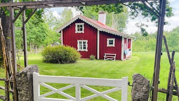 A red wooden house with a white gate in front, surrounded by greenery.