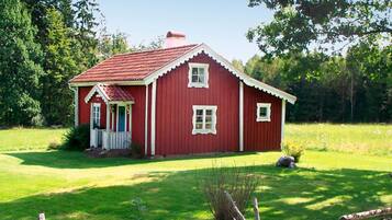 Una casa de madera roja con un porche, rodeada por un campo cubierto de césped y árboles.