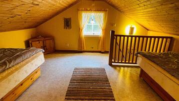 A cozy attic bedroom with two wooden beds, a small nightstand, a window with curtains, and a wooden railing.