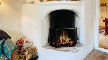 A fireplace with a fire, a wall with floral wallpaper, and a chair with a patterned cover.