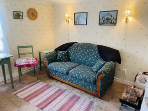 Una sala acogedora con un sofá estampado, una mesita, una silla y un tapete decorativo.