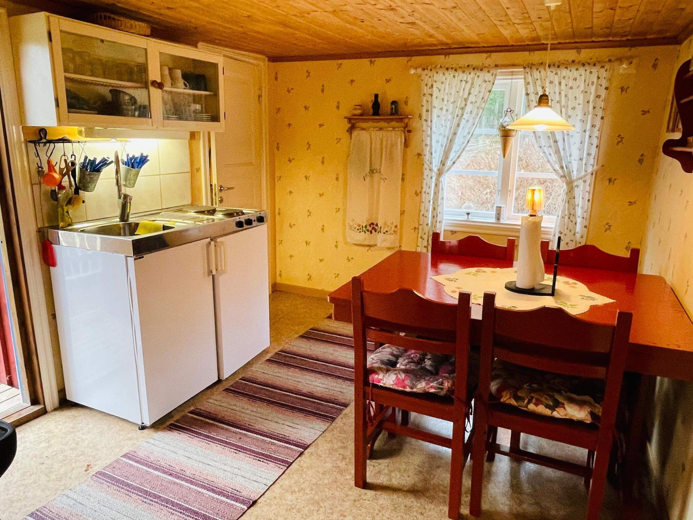 A compact kitchen with a dining area, wooden ceiling, and patterned wallpaper.