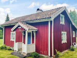 A red wooden house with a white porch and a blue door. - 4 Person Holiday Home in Skruv (Skruv)