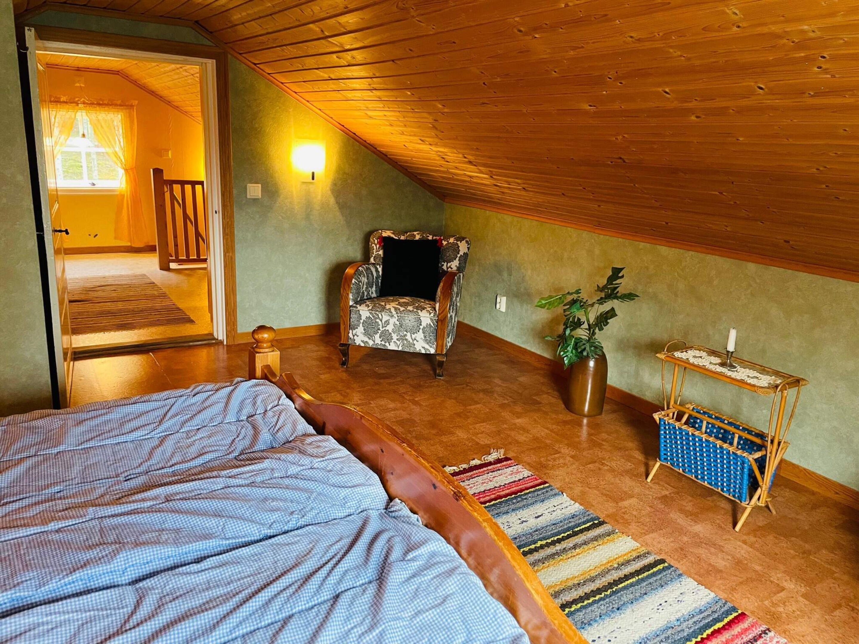 A cozy attic bedroom with a bed, a chair, a small table, and a potted plant.