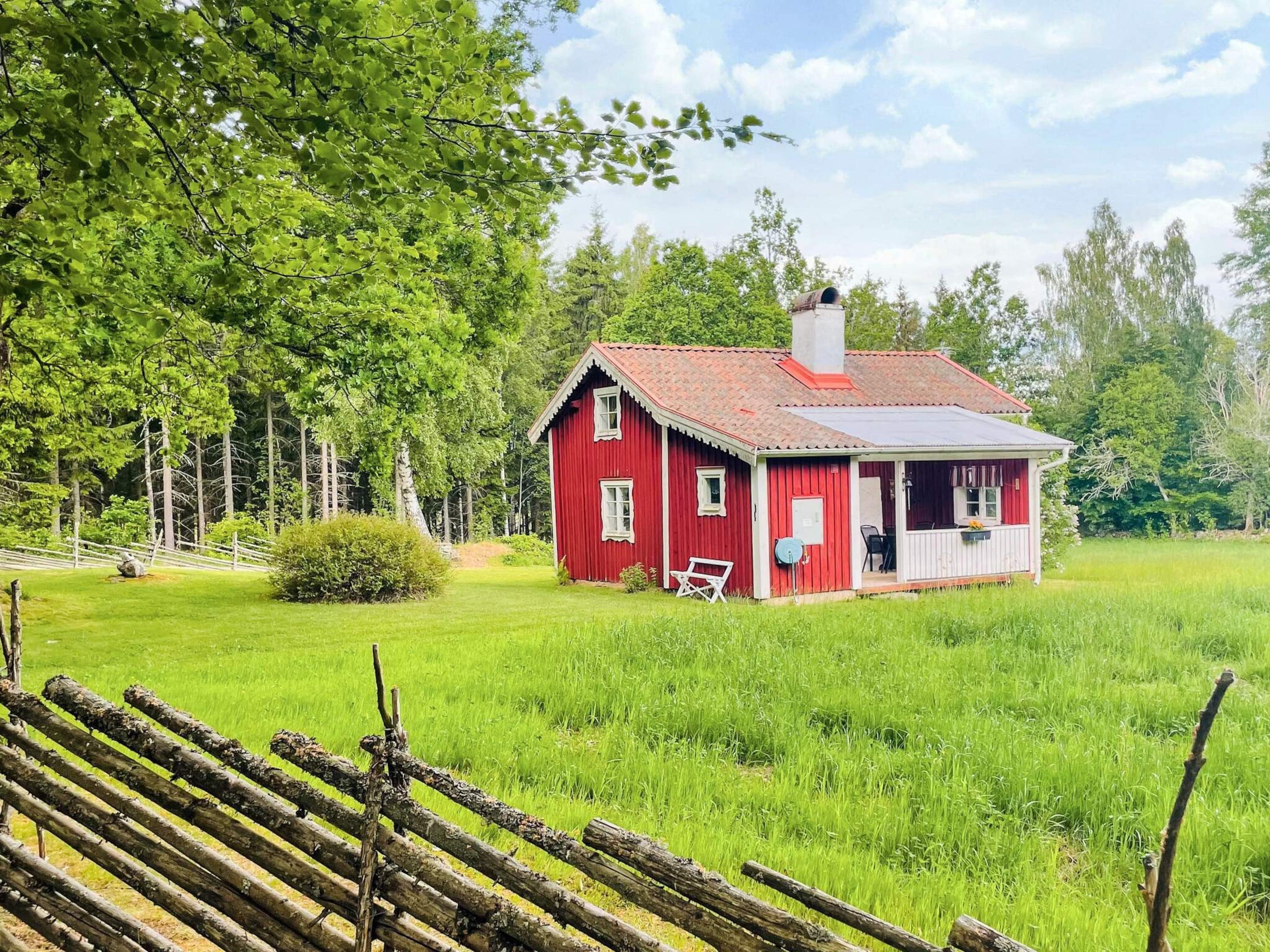 A red wooden house with a white porch, surrounded by a grassy field and trees.
