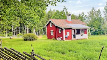 A red wooden house with a white porch, surrounded by a grassy field and trees.