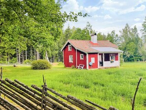 Una casa de madera roja con un porche blanco, rodeada de un campo cubierto de pasto y árboles.
