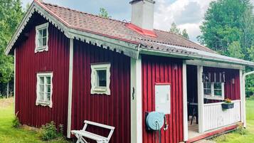 A red wooden house with a white porch, a bench, and a water pump.