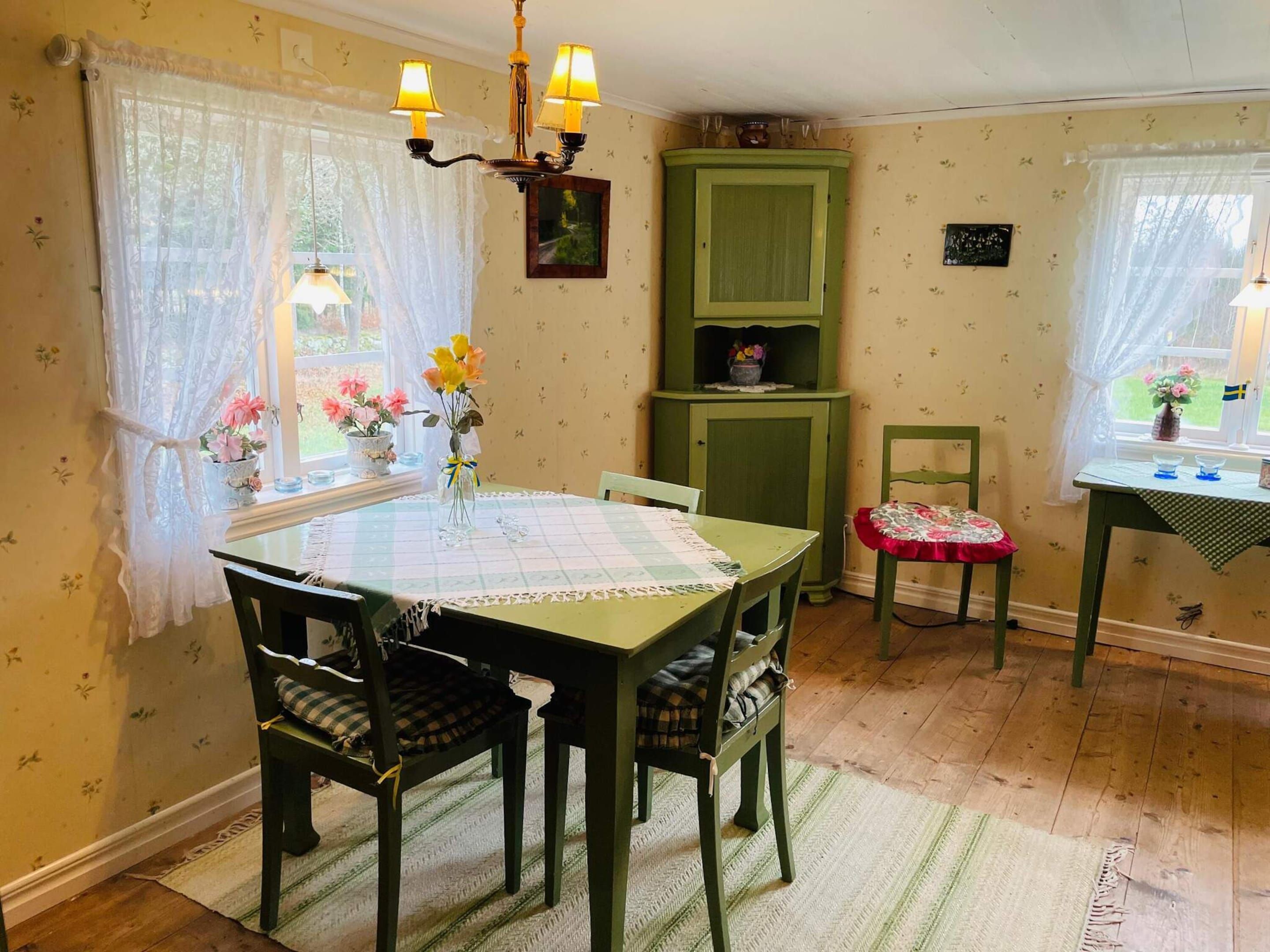A dining area with a table, chairs, a chandelier, a cabinet, and a window with curtains.