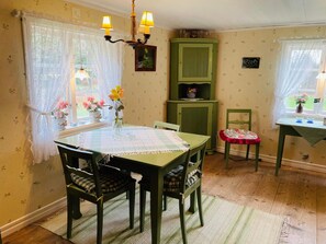 Un comedor con una mesa, sillas, una araña, un armario y un ventanal con cortinas.
