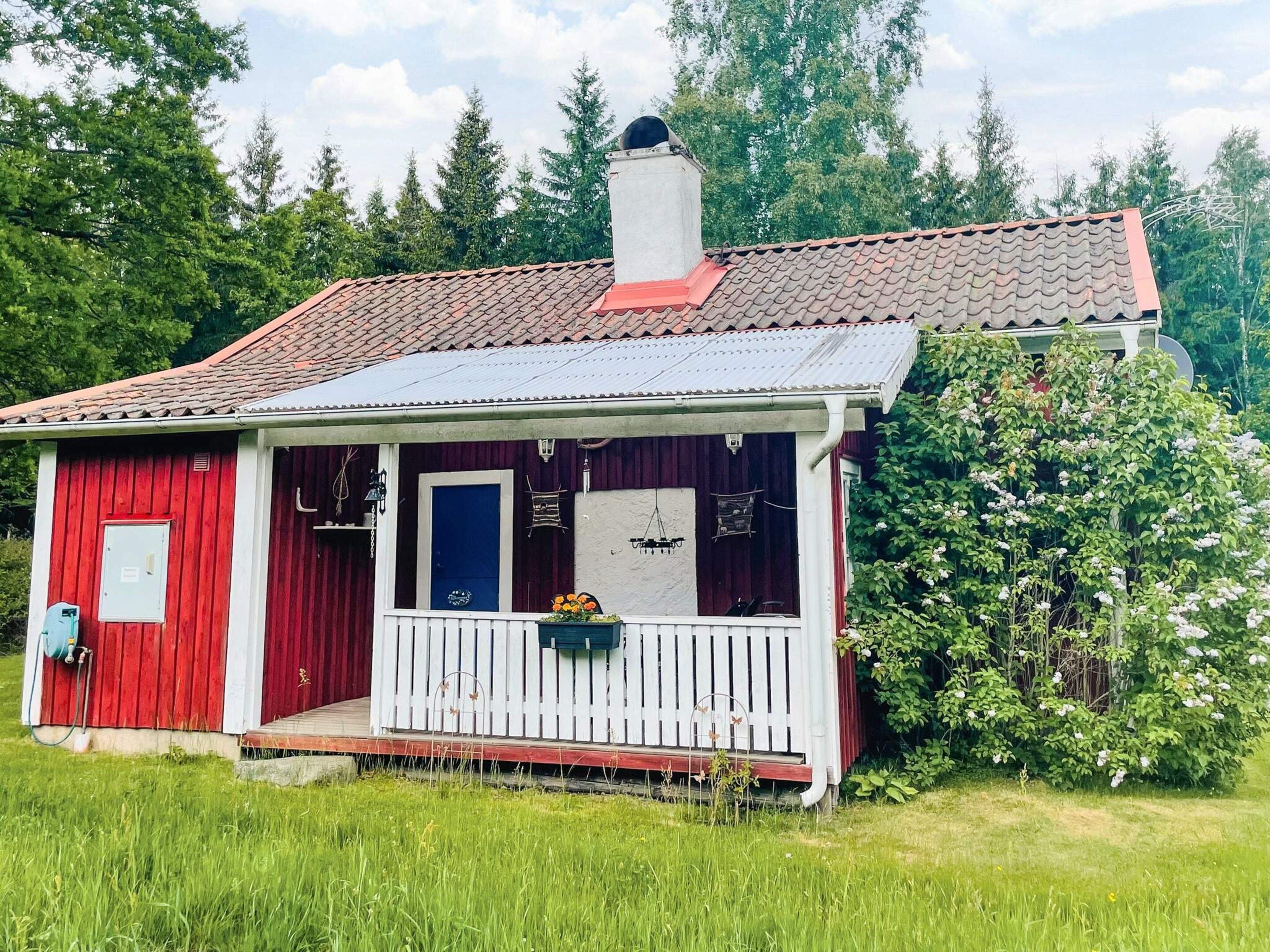 A red wooden house with a white porch, a chimney, and a garden.
