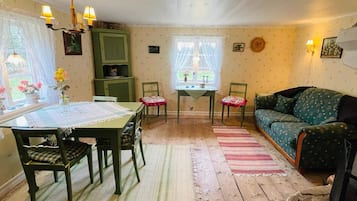 A cozy living room with a green sofa, a dining table with chairs, and a small table with a vase of flowers.