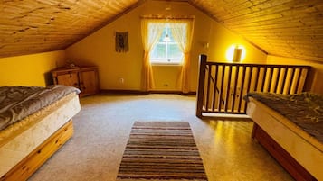 A cozy attic bedroom with two wooden beds, a small nightstand, a window with curtains, and a wooden railing.