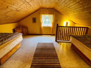 A cozy attic bedroom with two wooden beds, a small nightstand, a window with curtains, and a wooden railing. - 4 Person Holiday Home in Skruv (Skruv)