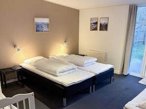 A hotel room with two beds, a desk, and a chair. There are two wall-mounted lamps and two framed pictures on the wall.
