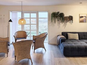 A living room with wicker furniture, a dark sofa, and a view through a large window. - 4 Star Holiday Home in Harboore (Harboore)