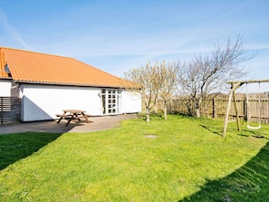 A house with a red-tiled roof, a white exterior, and a wooden swing set in the backyard.