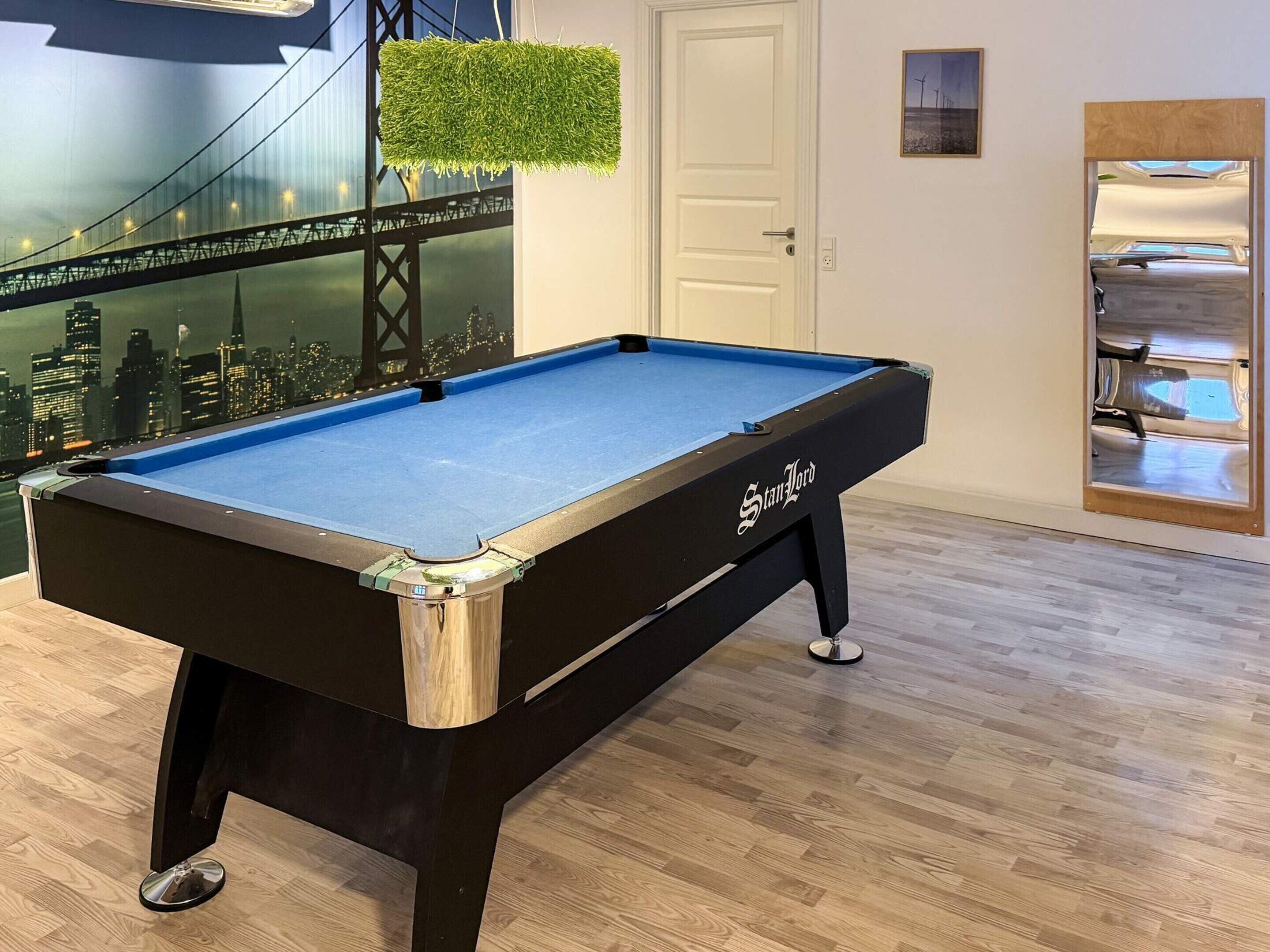 A pool table with a cityscape mural in the background, a door, and a mirror reflecting a car.