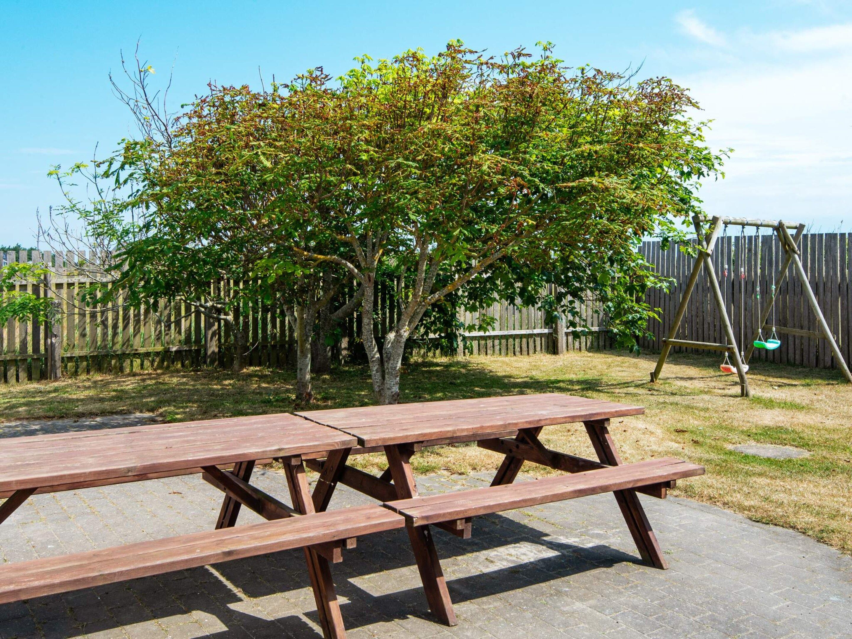 A picnic table in a backyard with a wooden fence and a swing set.