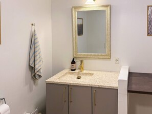 A bathroom with a beige countertop, a gold faucet, a mirror with a gold frame, and a towel hanging on a rack.