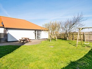 Une maison avec un toit recouvert de tuiles rouges, une balançoire en bois et une table de pique-nique dans le jardin.