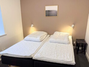A double bed with white bedding and two bedside lamps, a small table with a chair, and a framed picture on the wall. - 4 Star Holiday Home in Harboore (Harboore)