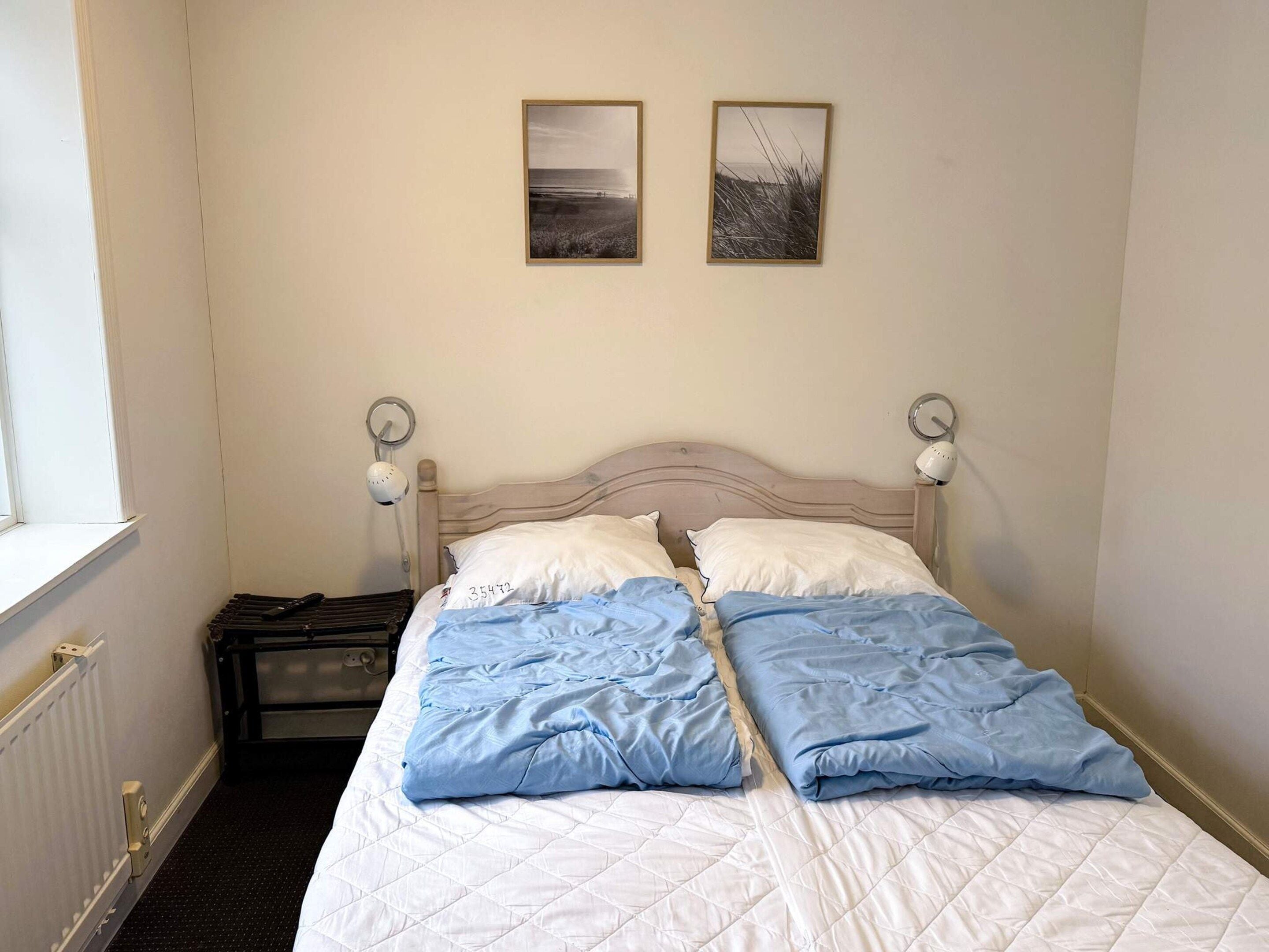 A double bed with a white and blue duvet, two bedside lamps, and two framed pictures on the wall.