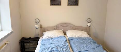 A double bed with a white and blue duvet, two bedside lamps, and two framed pictures on the wall.