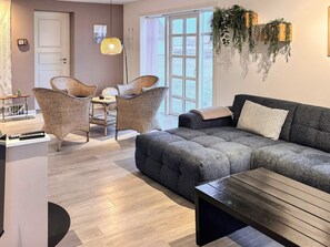 Una sala de estar moderna con un sofá gris, sillas de mimbre, una mesa de centro de madera y un ventanal con vistas.