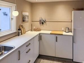 A modern kitchen with a window, a hanging light, a knife rack, and a refrigerator.