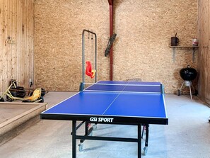 Una mesa de ping pong con ruedas, una silla colgante y una parrilla de barbacoa en una habitación con paredes de madera.