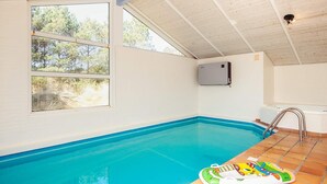 An indoor swimming pool with clear blue water, a tiled floor, and a window providing a view of trees. - 10 Person Holiday Home in Blavand (Blavand)