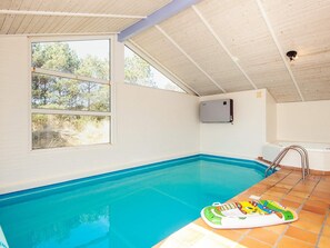 An indoor swimming pool with clear blue water, a tiled floor, and a window providing a view of trees. - 10 Person Holiday Home in Blavand (Blavand)