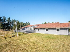 A single-story house with a red-tiled roof, a fenced yard, and a swing set. - 10 Person Holiday Home in Blavand (Blavand)
