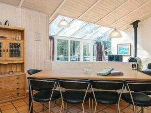 A dining area with a large table, six black chairs, a wooden cabinet, and a large window with a view of trees. - 10 Person Holiday Home in Blavand (Blavand)