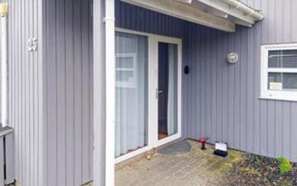 A house with a grey exterior, a white door, and a small garden area with a red object and a black bag. - 10 Person Holiday Home in Blavand (Blavand)