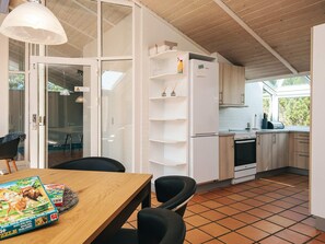 A modern kitchen with white cabinets, a built-in oven, and a dining area with a wooden table and chairs. - 10 Person Holiday Home in Blavand (Blavand)