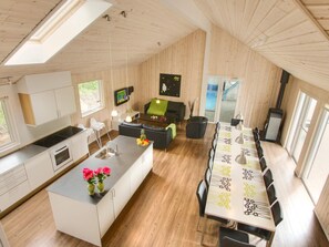 A modern kitchen with a central island, dining area with a long table, and a cozy seating area with a fireplace. - 5 Star Holiday Home in Ebeltoft (Ebeltoft)