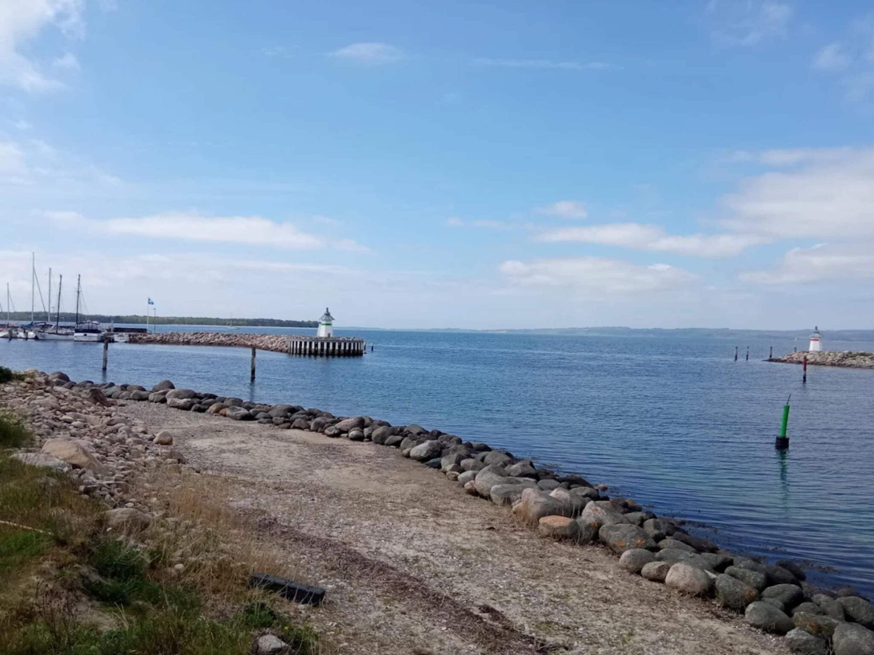 Eine Küstenlandschaft mit Leuchtturm, felsigem Ufer und ruhigem Wasser.