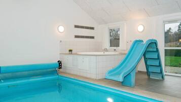 Ein Schwimmbecken mit Rutsche, kleinem Fenster und weiß gefliester Wand.