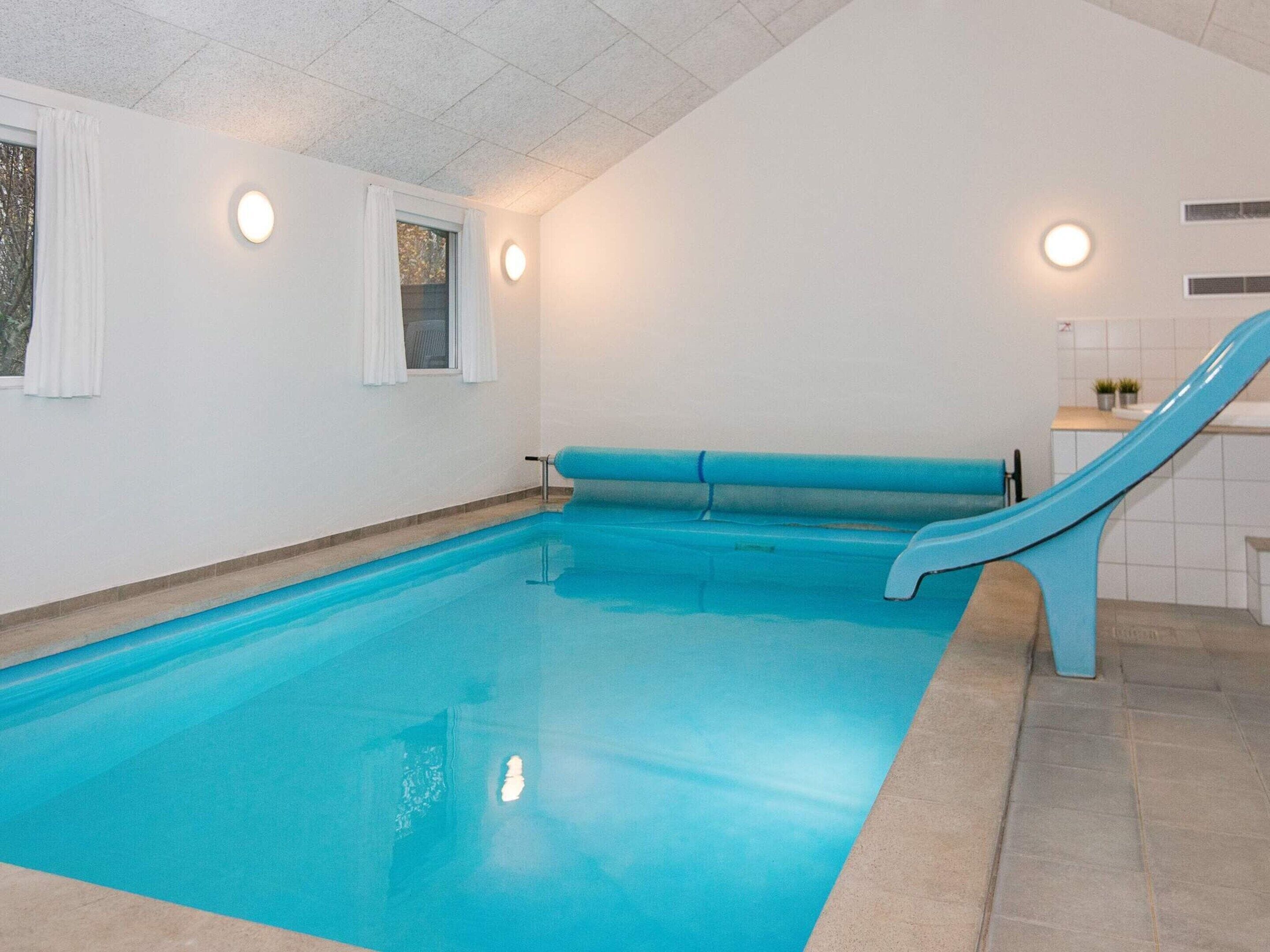 Una piscina con un tobogán azul, paredes blancas y piso de baldosas.