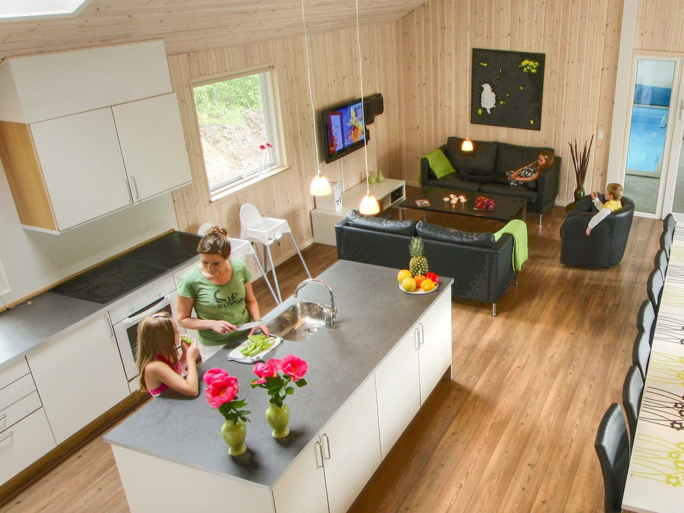 A modern kitchen with a central island, a dining area with a black sofa, and a living room with a television.