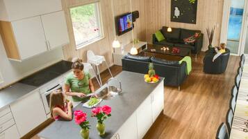 A modern kitchen with a central island, a dining area with a black sofa, and a living room with a television.
