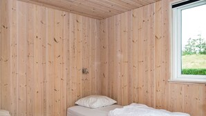 Un llit individual amb roba de llit blanca a una habitació amb parets de fusta i una finestra.