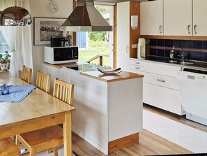 A compact kitchen with a dining area, a microwave, a sink, and a clock on the wall. - Holiday Home in SpekerÃ¶d (Spekeröd)