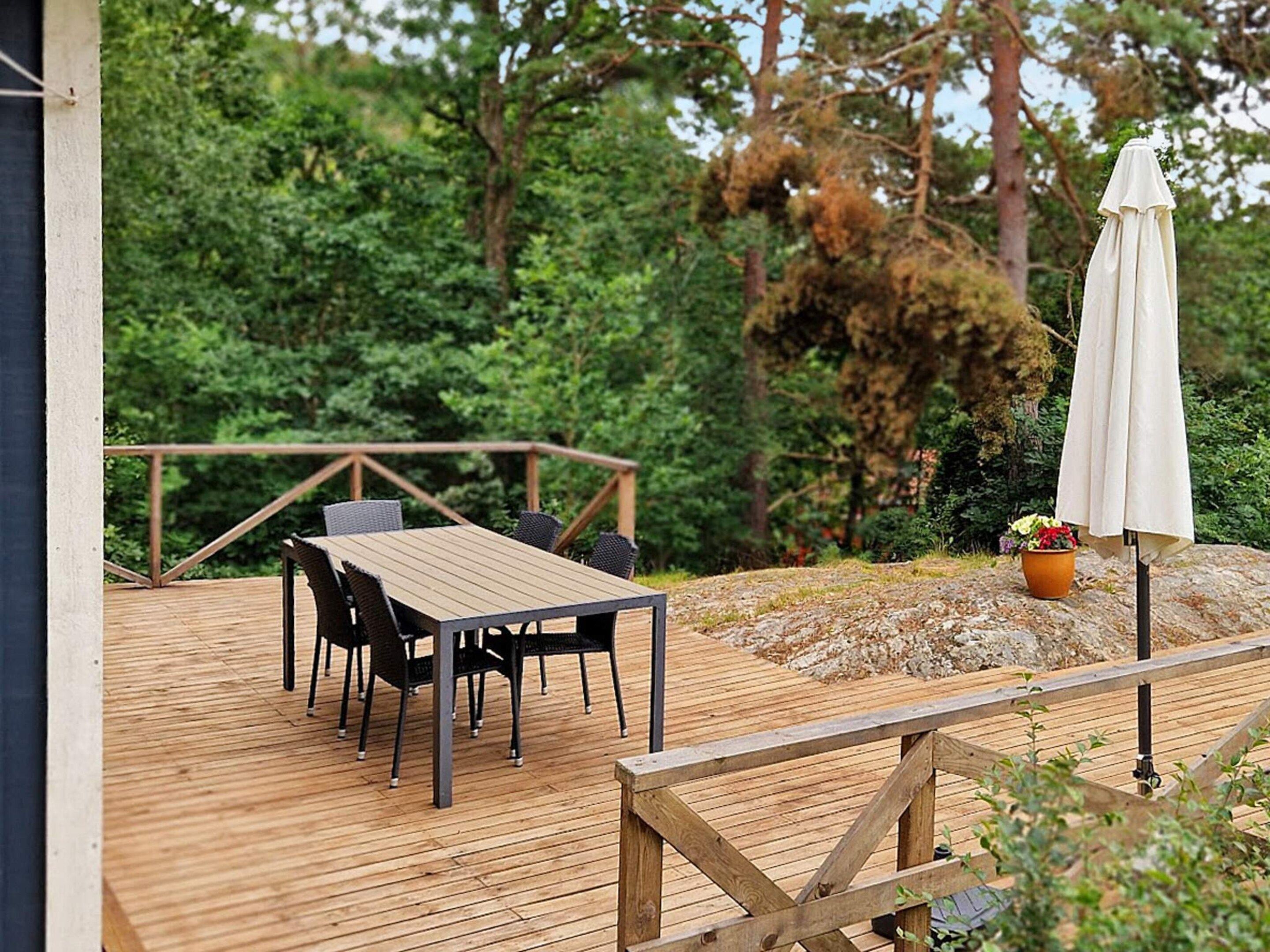 A wooden deck with a table and chairs, surrounded by greenery.