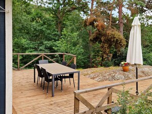 A wooden deck with a table and chairs, surrounded by greenery. - Holiday Home in SpekerÃ¶d (Spekeröd)