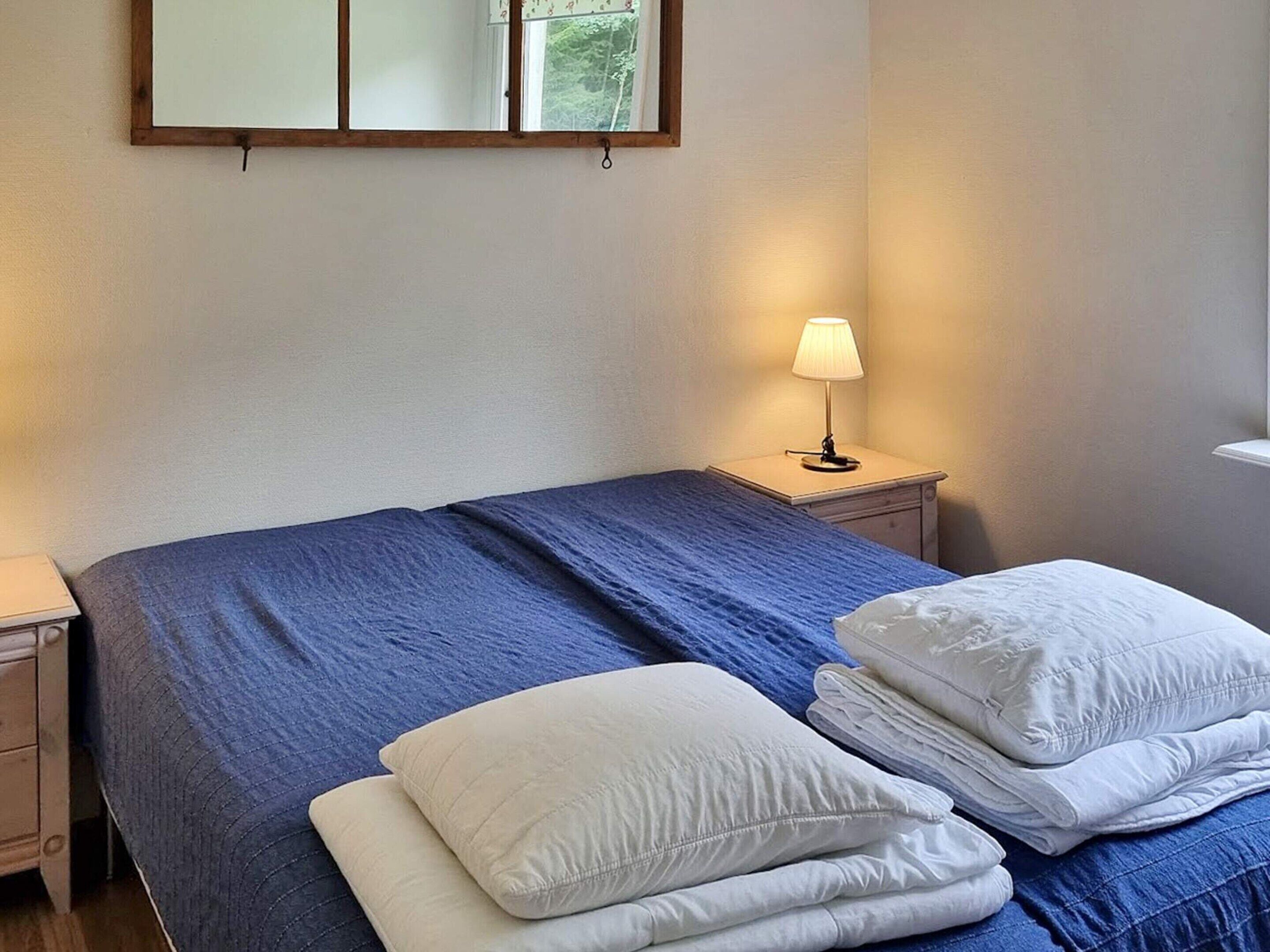 Habitación de hotel con cama, mesita de noche con lámpara y ventana con vistas a árboles.