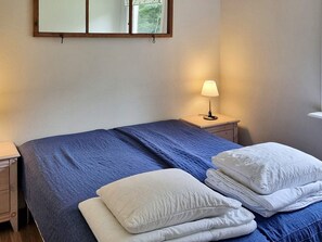 Een hotelkamer met een bed, een nachtkastje met een lamp en een raam met uitzicht op bomen.