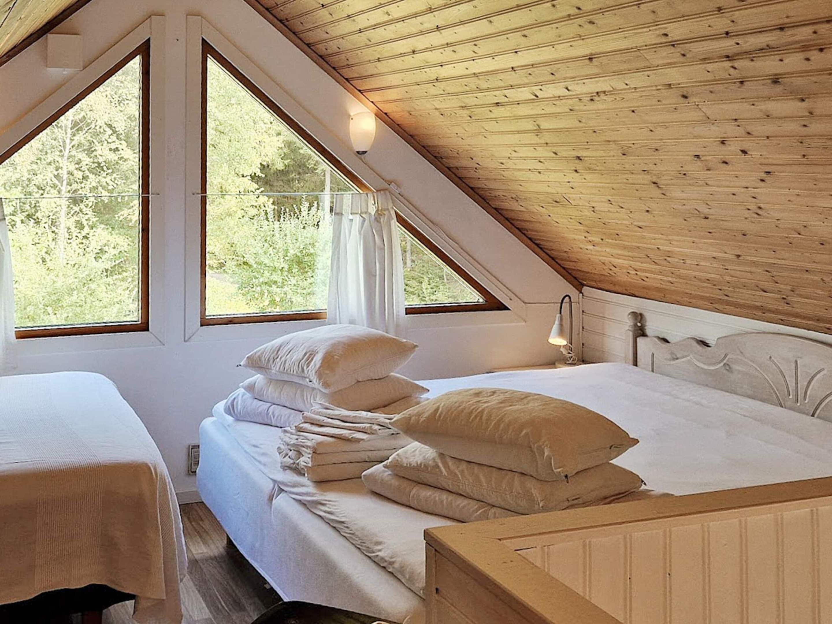 Une chambre avec un plafond en pente, deux lits et de grandes fenêtres.